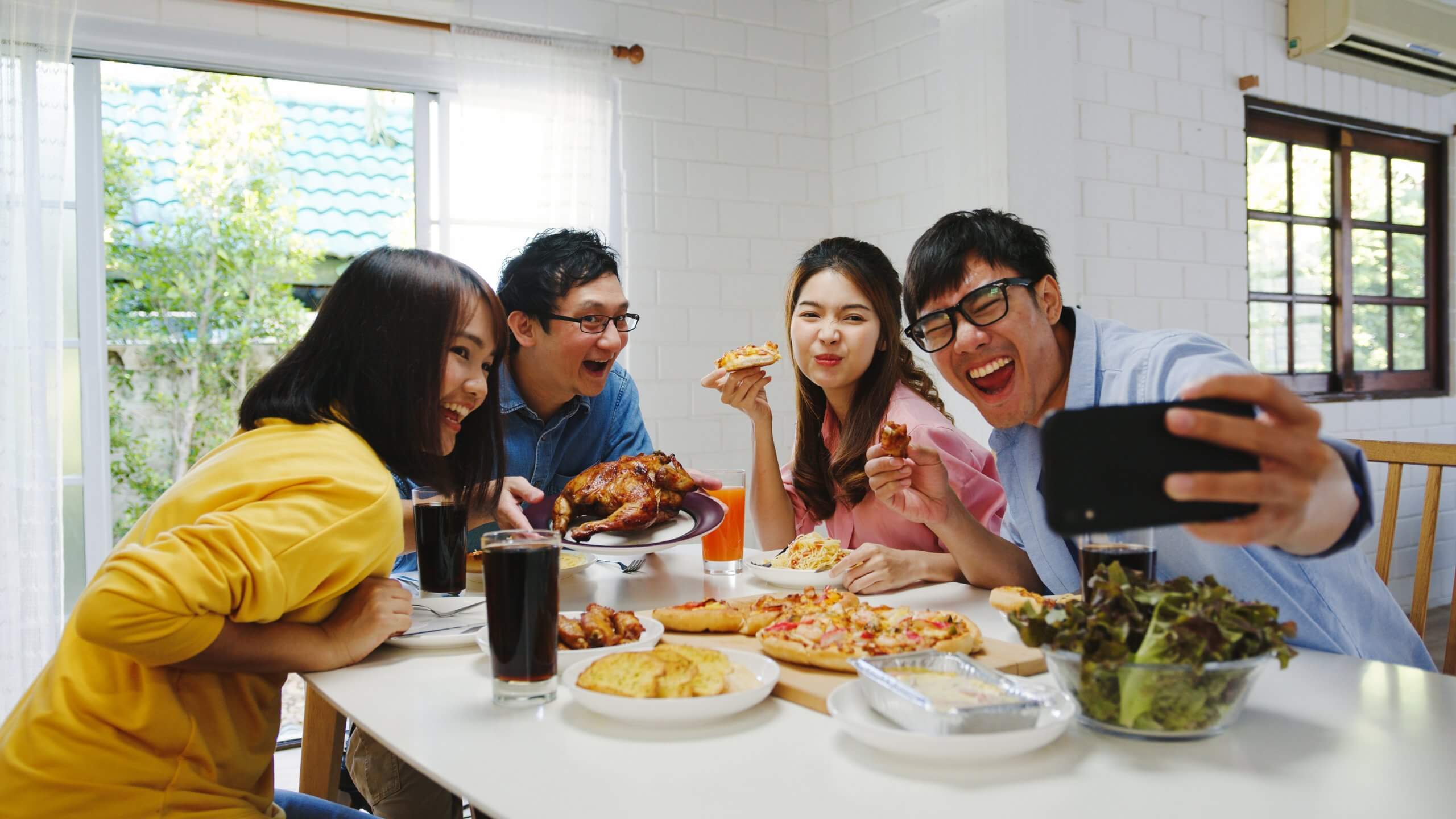 Happy young group having lunch at home. Asia family party eating pizza food and making selfie with her friends at birthday party at dining table together at house. Celebration holiday and togetherness